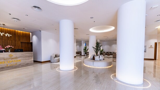 A modern reception area with a marble floor, large white columns, and a reception desk with a wooden panel backdrop. - Jasmine Garden Hotel Makkah (Makkah)