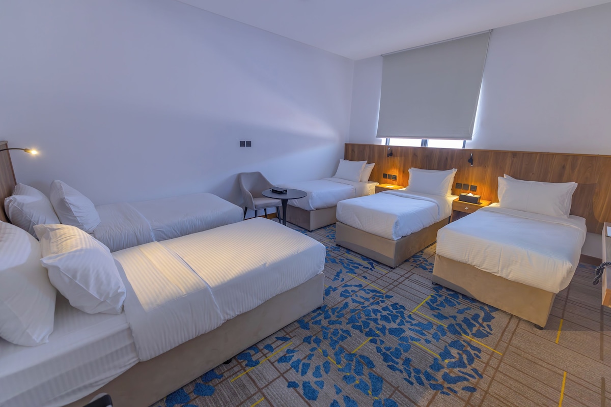 Een hotelkamer met twee éénpersoonsbedden, een slaapbank, een klein tafeltje en een stoel.