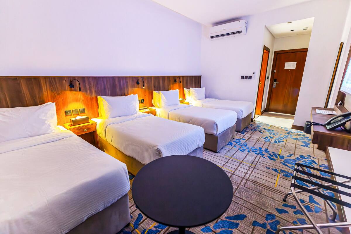 A hotel room with three beds, a small round table, and a desk with a telephone.