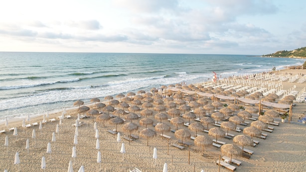 A beach with rows of sun loungers and thatched umbrellas, a lifeguard tower, and a sandy shoreline. - Casa dell'Eleganza Event Hall & Hotel (Kranevo)