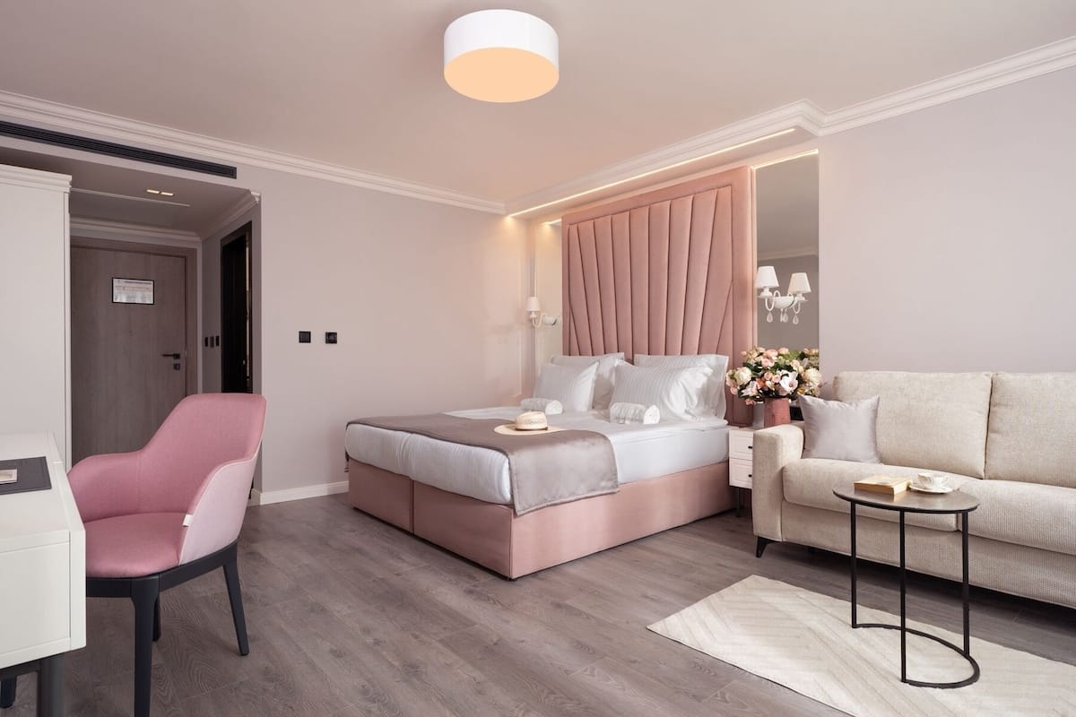 A modern bedroom with a bed, a pink chair, a sofa, and a small table.