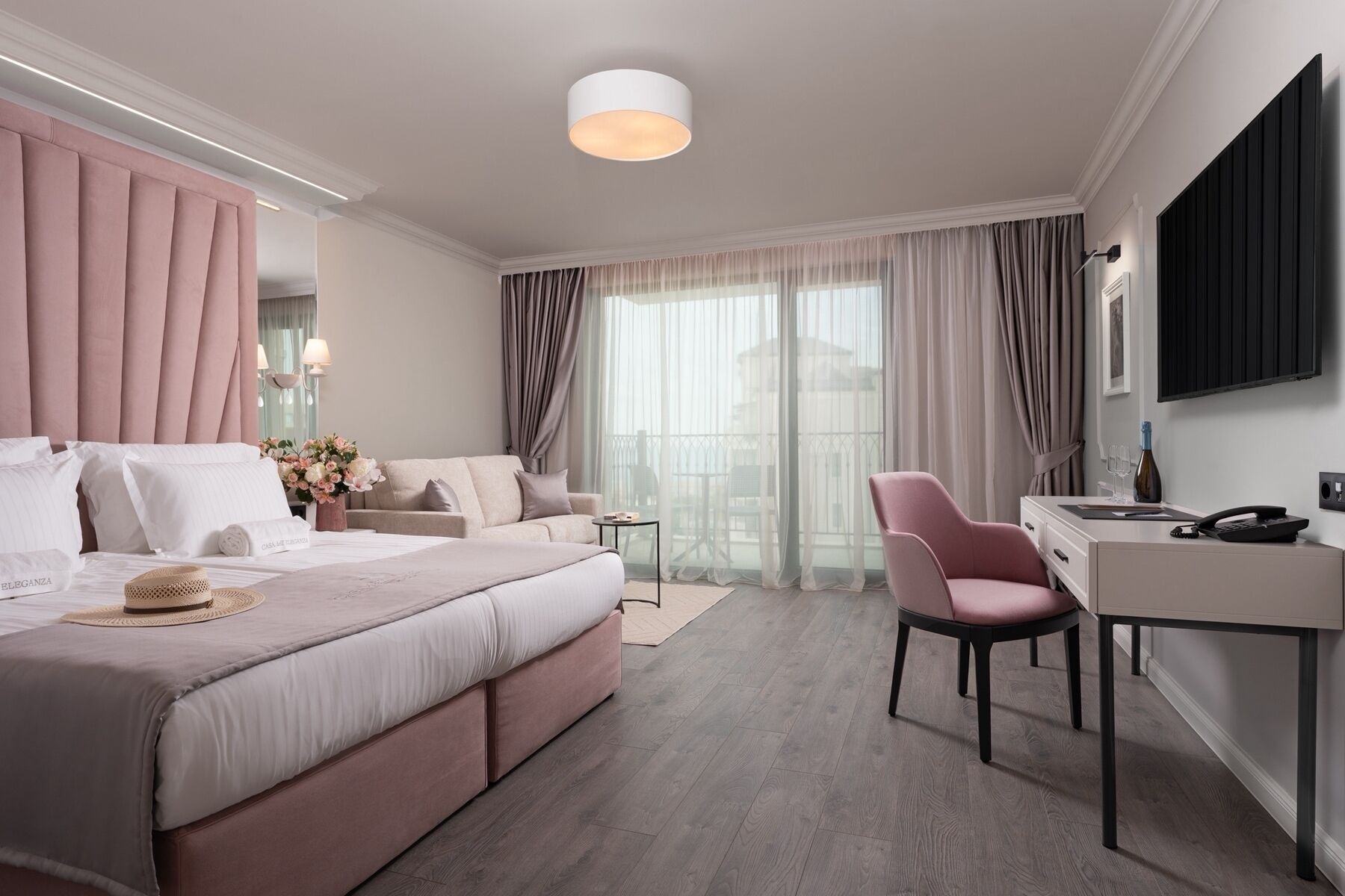 A modern hotel room with a large bed, a desk, a chair, and a TV.