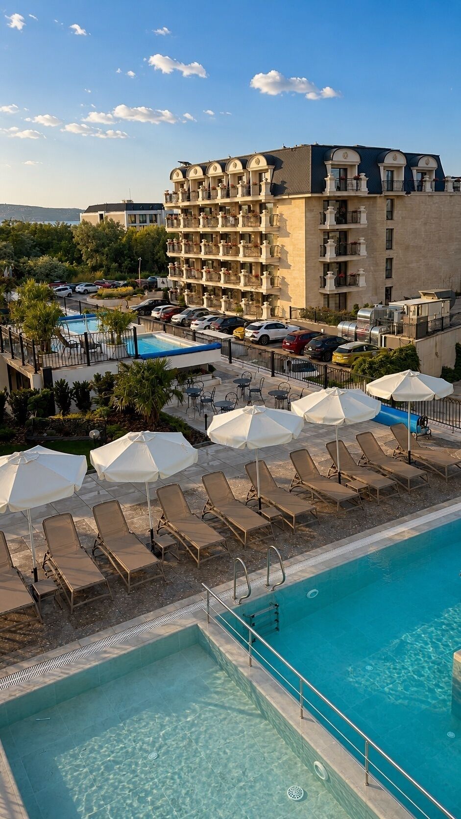 A hotel with a swimming pool, sun loungers, umbrellas, and a view of the sea.