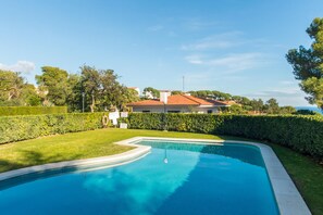 A swimming pool with a curved edge, surrounded by well-maintained grass and hedges, with a house and trees in the background. - K-8 Apartment with wonderful sea views (Calella de Palafrugell)