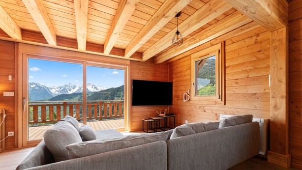 Ein Holzinterieur mit einer Couch, einem Fernseher und einem Balkon mit Bergblick.