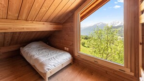 Ein Zimmer aus Holz mit einem Bett, einem Fenster und Blick auf Berge.