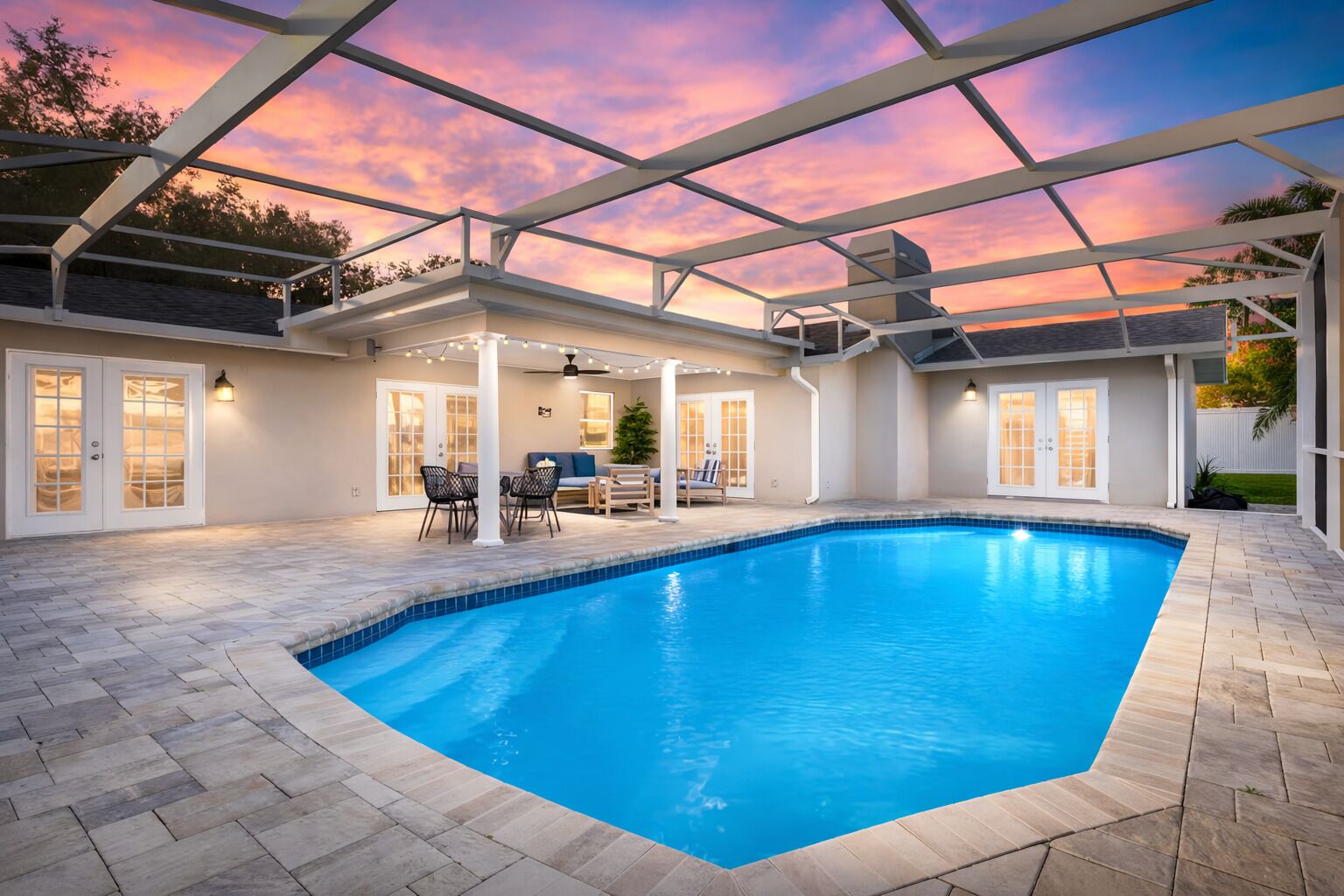 Una piscina con un porche techado, mobiliario exterior y vista al océano al atardecer.