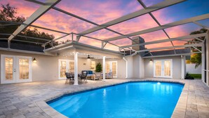A swimming pool with a covered patio area, outdoor seating, and a view of the ocean at sunset. - Sunshine, Salt Air & Poolside Living Awaits (Seminole)