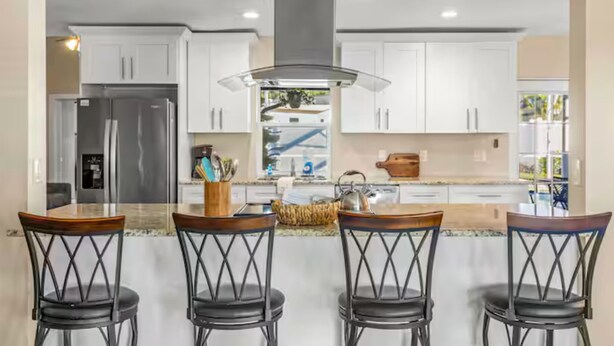 A modern kitchen with white cabinets, a stainless steel refrigerator, and a central island with bar stools. - Sunshine, Salt Air & Poolside Living Awaits (Seminole)