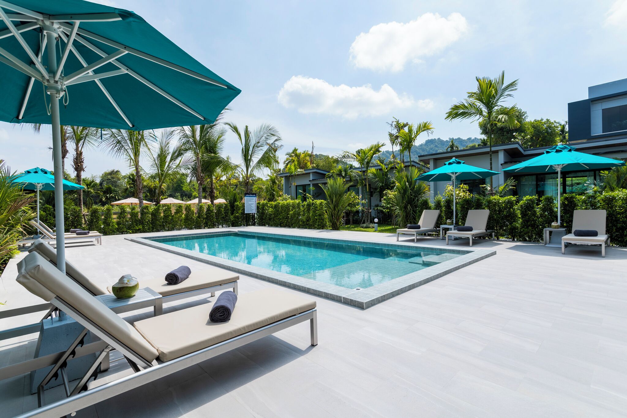 A swimming pool with lounge chairs and umbrellas, surrounded by greenery and modern buildings.