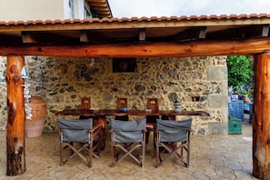 An outdoor wooden table with chairs under a wooden pergola, set against a stone wall with a rustic aesthetic. - Kliton Villa (5GH7+85F Dhrimiskos, Greece)