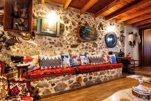 A stone-walled room with a wooden ceiling, a sofa with patterned cushions, a painting, and a mirror. - Kliton Villa (5GH7+85F Dhrimiskos, Greece)