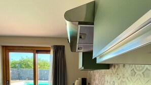 A kitchen with a built-in stove, a sink, and a view of a swimming pool through a glass door. - Gianna House and Choirs (Sicilia)
