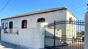 A white building with a tiled roof, a black metal gate, and a number '34' on the wall. - Gianna House and Choirs (Sicilia)