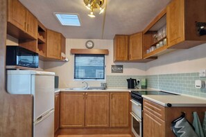 A compact RV kitchen with wooden cabinets, a sink, a stove, and a refrigerator. - Palm Court - 3 Bed, Heated Pool, Parking, Nr Beach (Par)