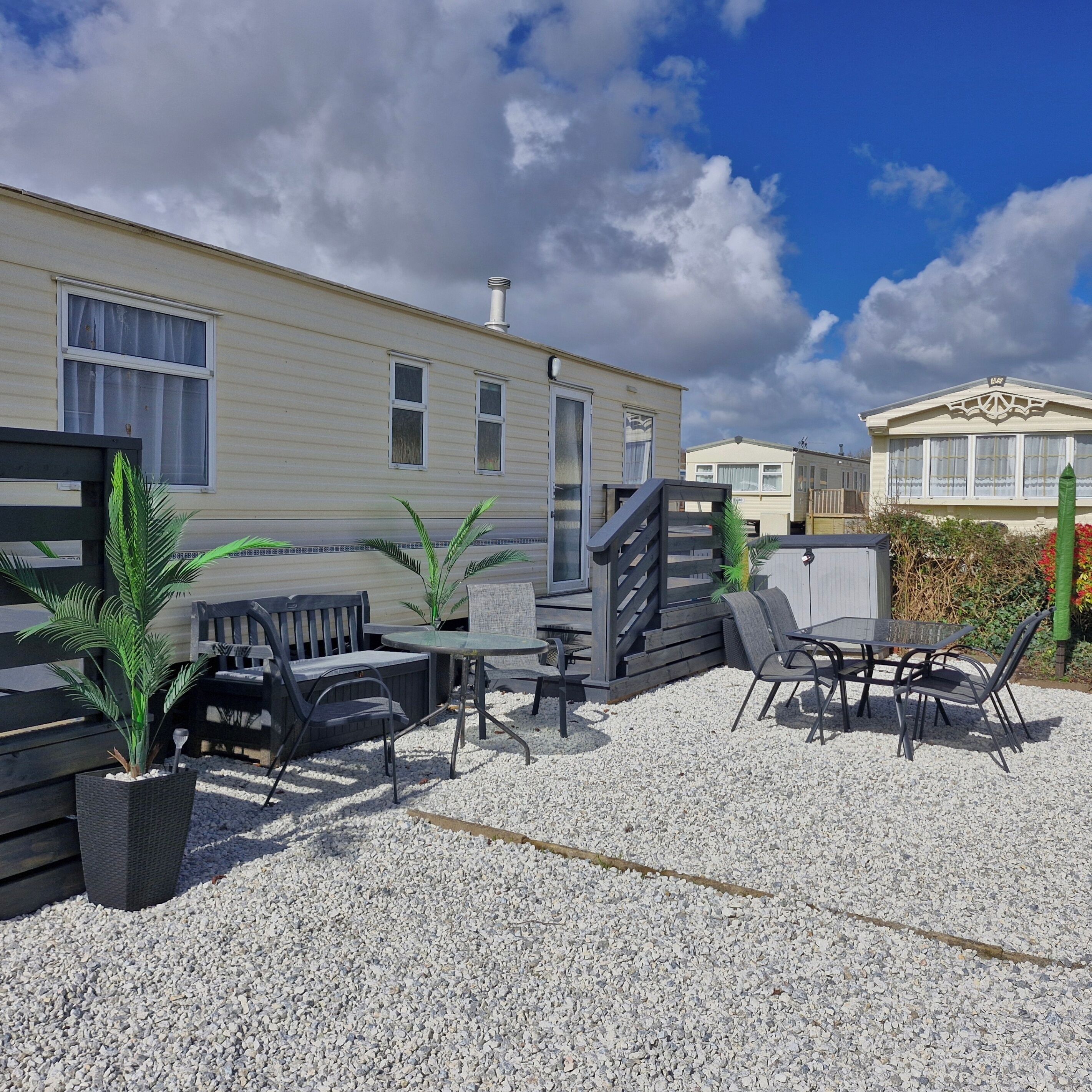 En campingvogn med udendørs siddepladser, en grusbelagt terrasse og udsigt til himlen.