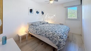 Un dormitorio con cama, ventilador de techo, mesita de noche, ventana y decoración en la pared.