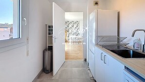 Una cocina estrecha con una ventana, un cubo de basura, un refrigerador y un lavaplatos.