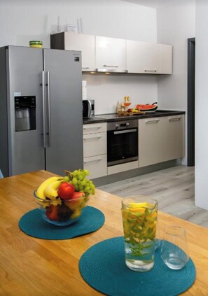 A modern kitchen with a refrigerator, oven, and microwave. There is a fruit bowl on the table and a glass of water. - Villa Venka – Luxury Villa for 8-10 Guests with Private Pool in Central Rab (Palit)
