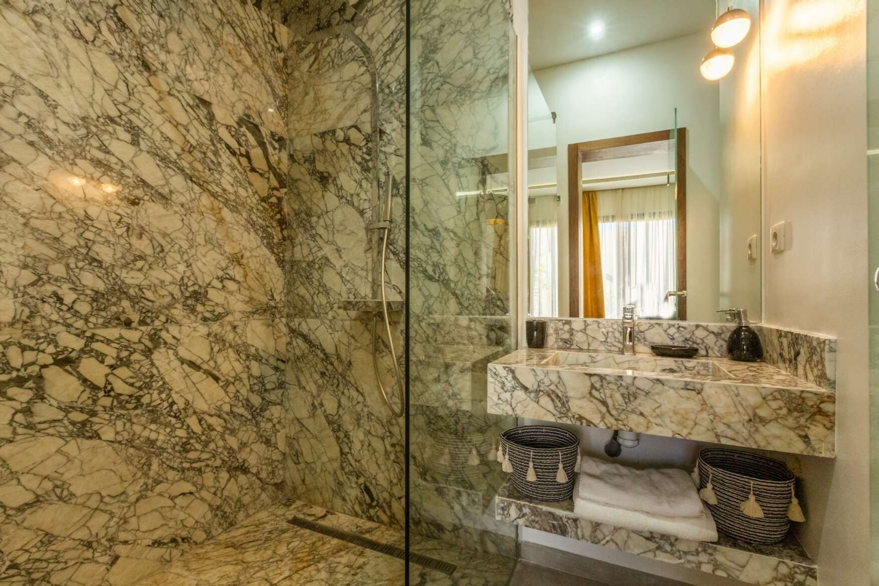A bathroom with a marble shower and a vanity with a mirror.