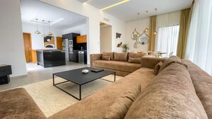Ein modernes Wohnzimmer mit einem großen beigefarbenen Sofa, einem schwarzen Couchtisch und einer Küche im Hintergrund.
