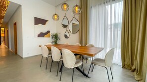 Un coin repas comprenant une table en bois et six chaises, une plante en pot et trois lampes suspendues fixées au mur.
