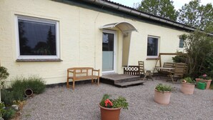 A house with a porch, a bench, a table, and chairs. There are potted plants and a gravel driveway. - At the meadow (Kuchelmiß)