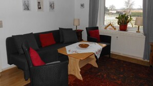 A living room with a black sofa, red cushions, a small wooden table, and a view of a snowy landscape through a window. - At the meadow (Kuchelmiß)