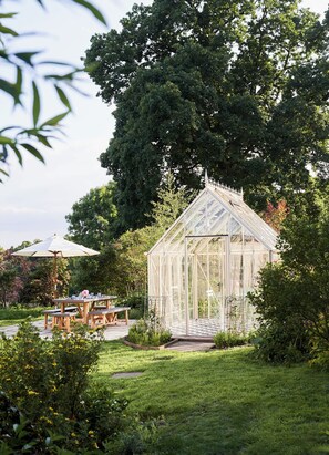 Une serre dotée d’un toit en verre, entourée d’un jardin où se trouvent une table de pique-nique et des bancs.