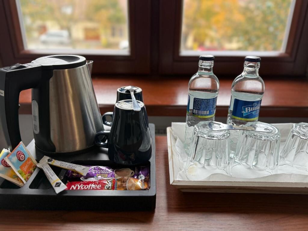 A coffee station with a coffee maker, cups, and coffee packets on a tray, and two bottles of Budweiser beer on a table.