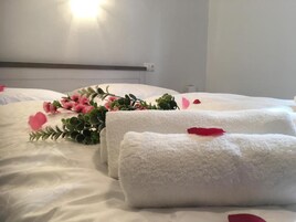 A neatly made bed with white linens, a red rose, and a small bouquet of pink flowers.
