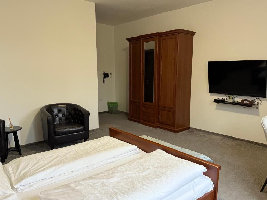 Quarto de hotel com cama, televisão, armário e uma cadeira.