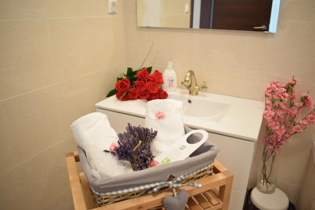 A bathroom with a white sink, a mirror above it, and a wooden stool with towels and flowers.