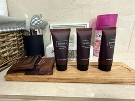 Una encimera de baño con productos para el cabello y el cuerpo, incluyendo dos tubos de Botanica con aceite de argán, un recipiente rosa y una cesta de mimbre.