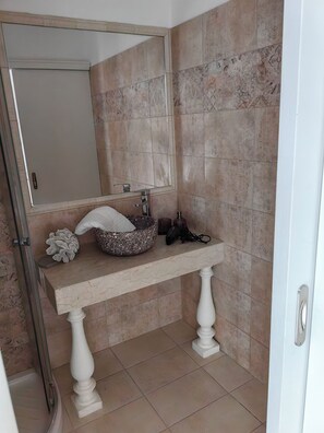Un baño con lavamanos de mármol, un espejo grande y zona de ducha.
