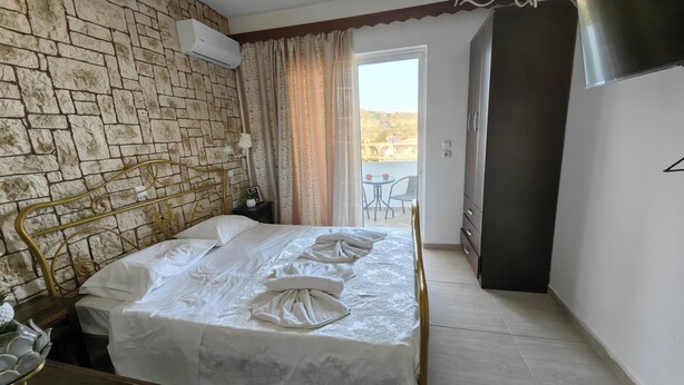 Ein Hotelzimmer mit Steinwand, einem Bett mit ordentlich gefalteten Handtüchern, einem Kleiderschrank und einem Balkon mit Aussicht.