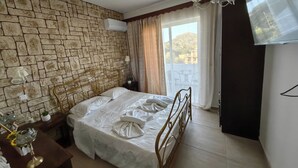 Ein Hotelzimmer mit Steinwand, einem Bett mit weißer Bettwäsche, einem Nachttisch mit Lampe und einem an der Wand befestigten Fernseher.