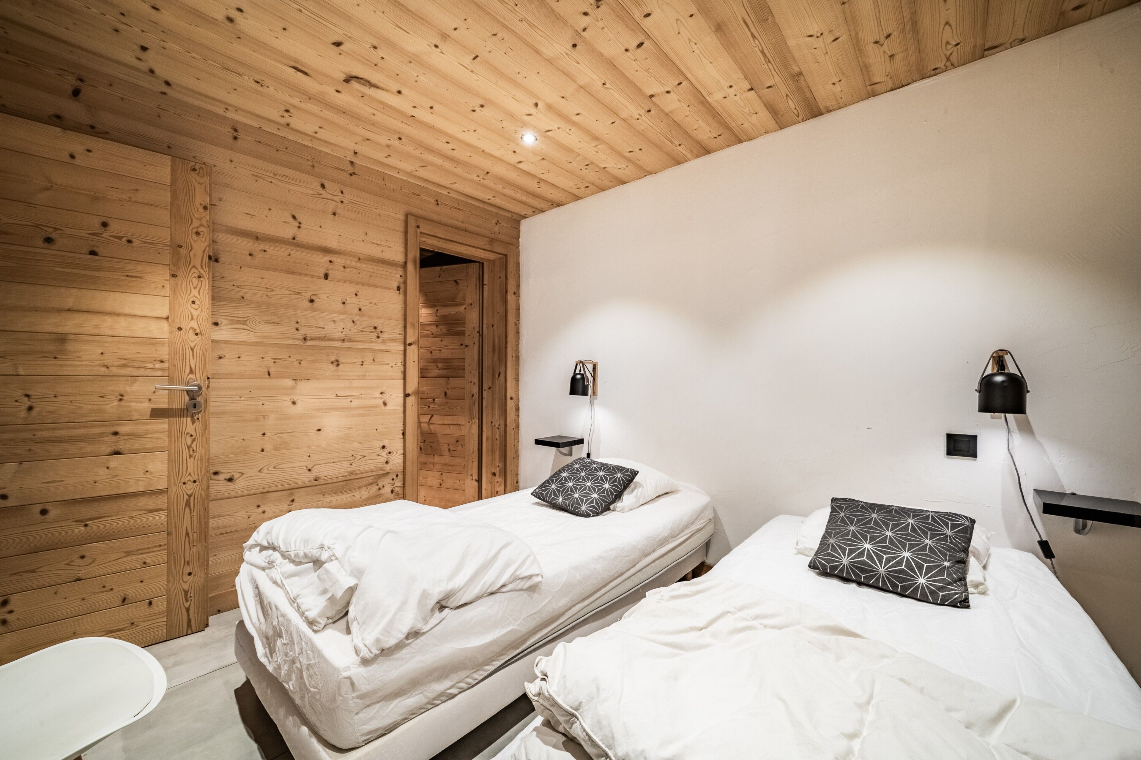 Una stanza con due letti, pareti in legno, una porta bianca e un piccolo tavolo bianco.