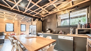 Eine moderne Küche mit Holzbalken, einem Essbereich mit Holztisch und -stühlen sowie einem großen Fenster mit Blick auf Grünflächen.
