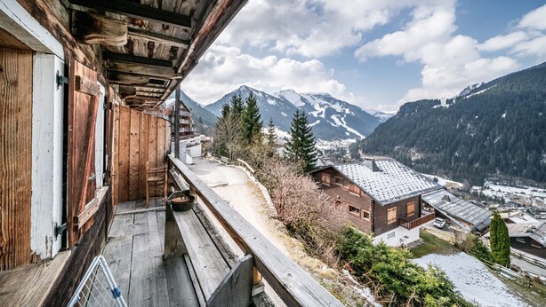 Ein Holzbalkon mit Blick auf ein Bergdorf und schneebedeckte Gipfel.