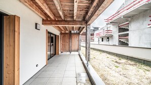 Een overdekte buitengalerij met houten balken, een betegelde vloer en uitzicht op een gebouw in aanbouw.