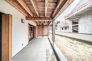Un corridoio esterno coperto con travi in legno, pavimento piastrellato e vista su un edificio in costruzione.