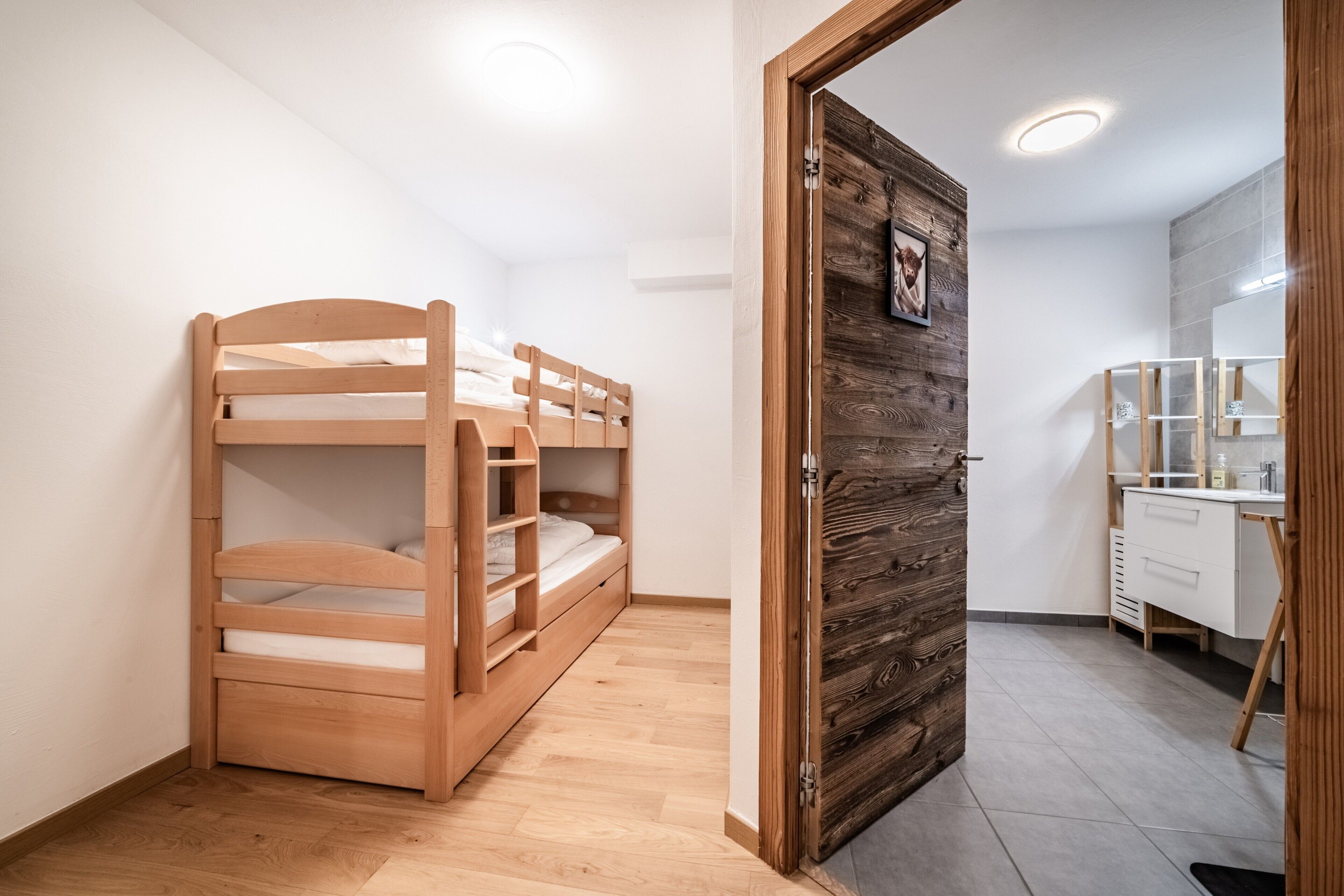 A bedroom with a bunk bed, a wooden door, a white dresser, and a mirror.