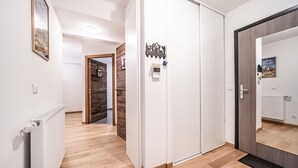 Een gang met een radiator, houten vloeren, een witte deur en een spiegel die een kamer met een radiator weerspiegelt.