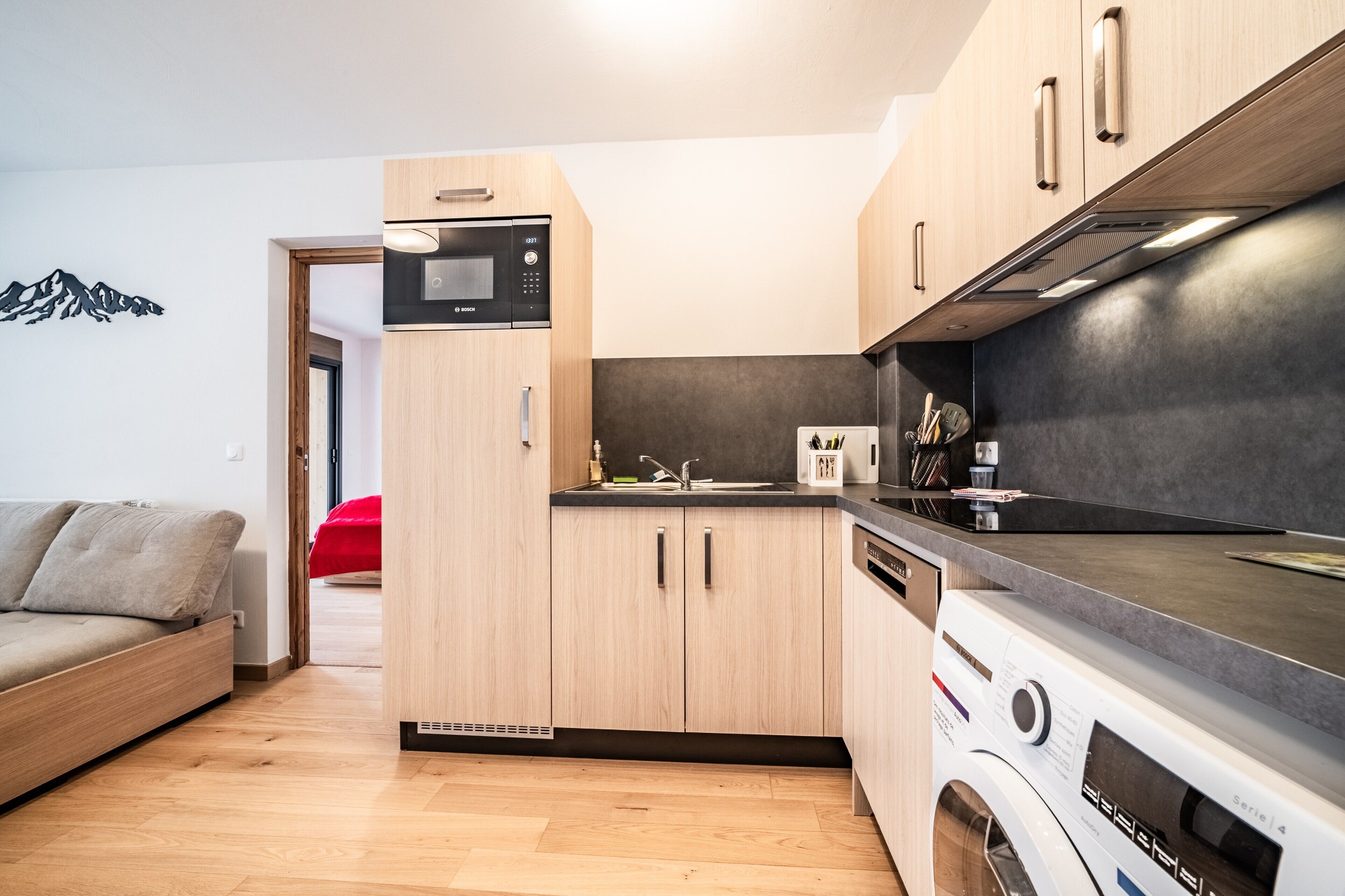Une cuisine compacte avec des meubles en bois, un four à micro-ondes encastré et un lave-linge à chargement frontal.