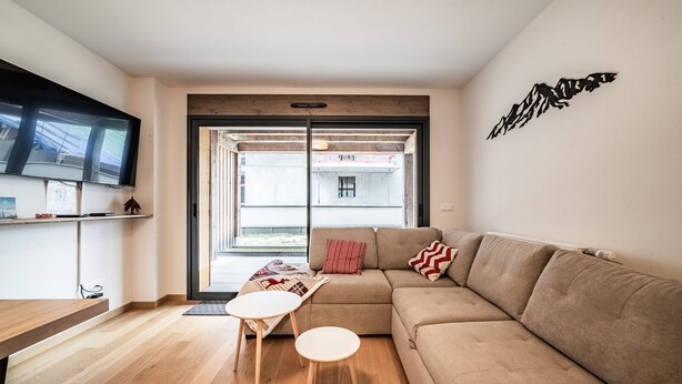 Een moderne woonkamer met een bank, een salontafel en een aan de muur bevestigde televisie.