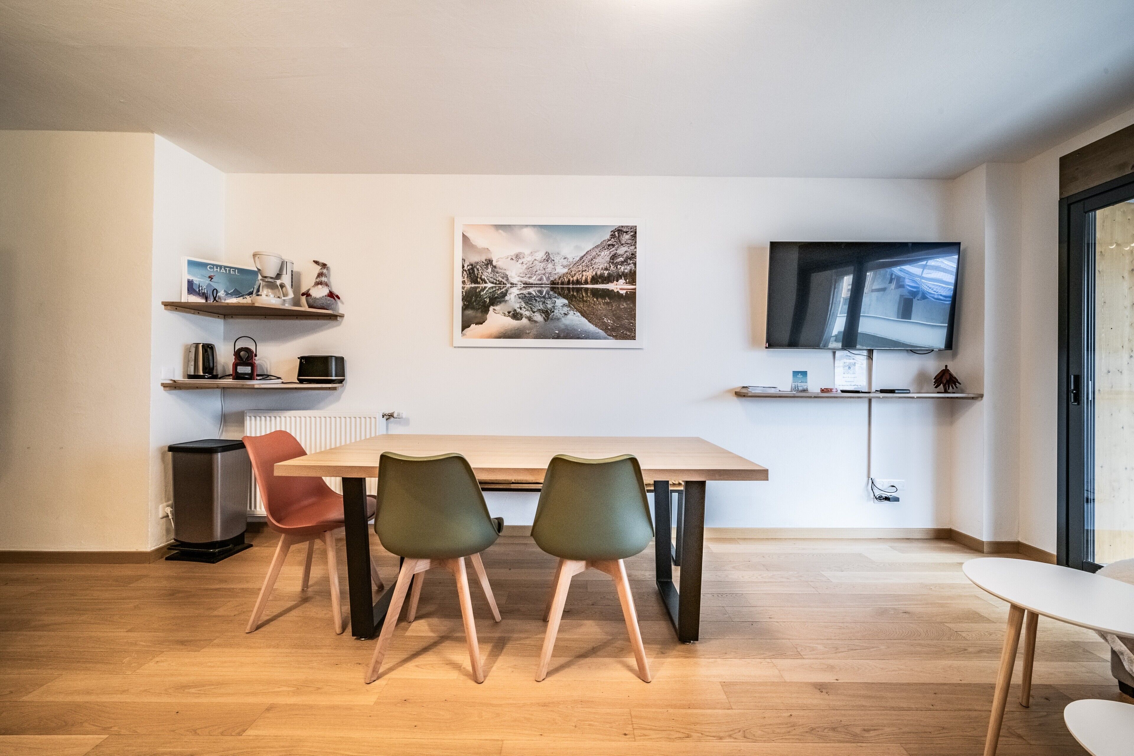 A modern dining area with a wooden table, two chairs, a TV, and a wall-mounted picture.