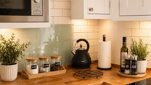 Een keuken met witte kastjes, een magnetron, een waterkoker en potten met suiker, theezakjes en koffie.