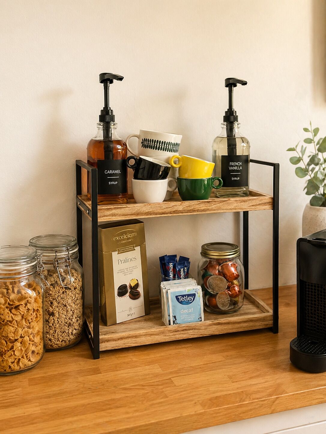 A wooden shelf with jars of granola, a box of pralines, a bottle of French vanilla syrup, and a coffee maker.