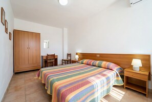 Un dormitori amb llit, taulella de nit, armari de fusta i escriptori amb cadira.